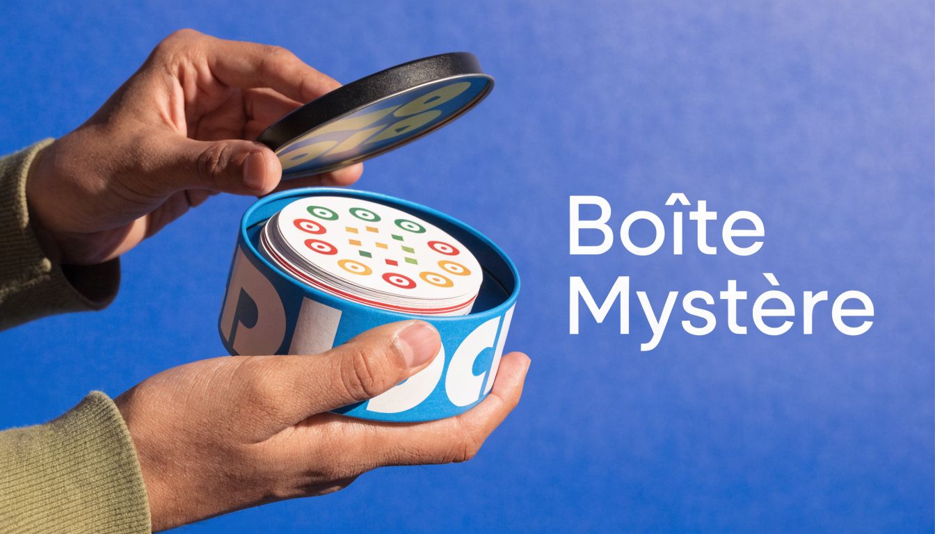 Mains tenant une boîte métallique ronde ouverte remplie de cartes de jeu colorées sur fond bleu.
